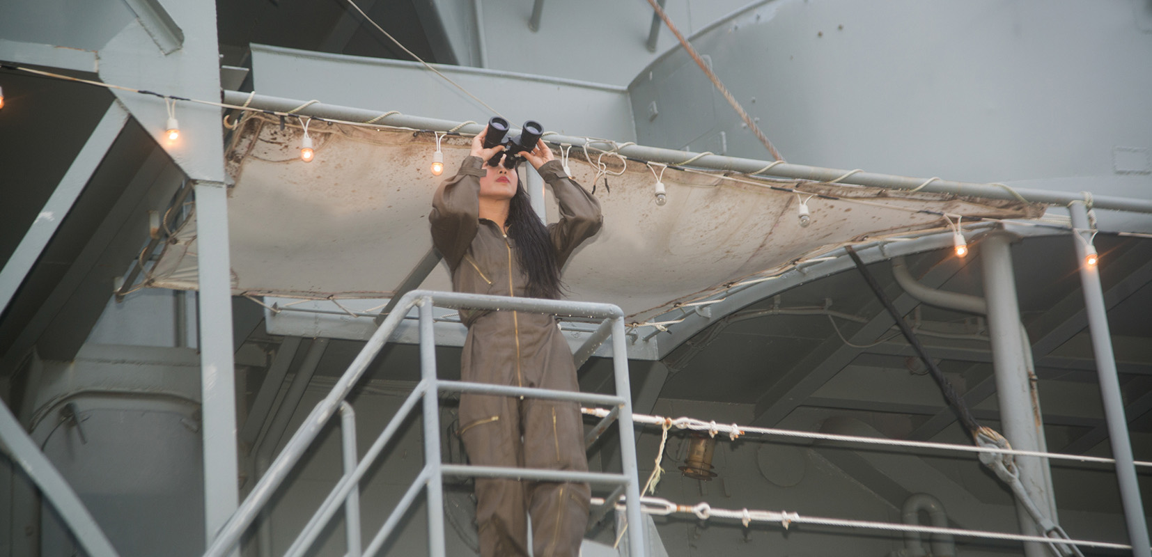 Mujer asiática en barco mercante mirando a través de binoculares