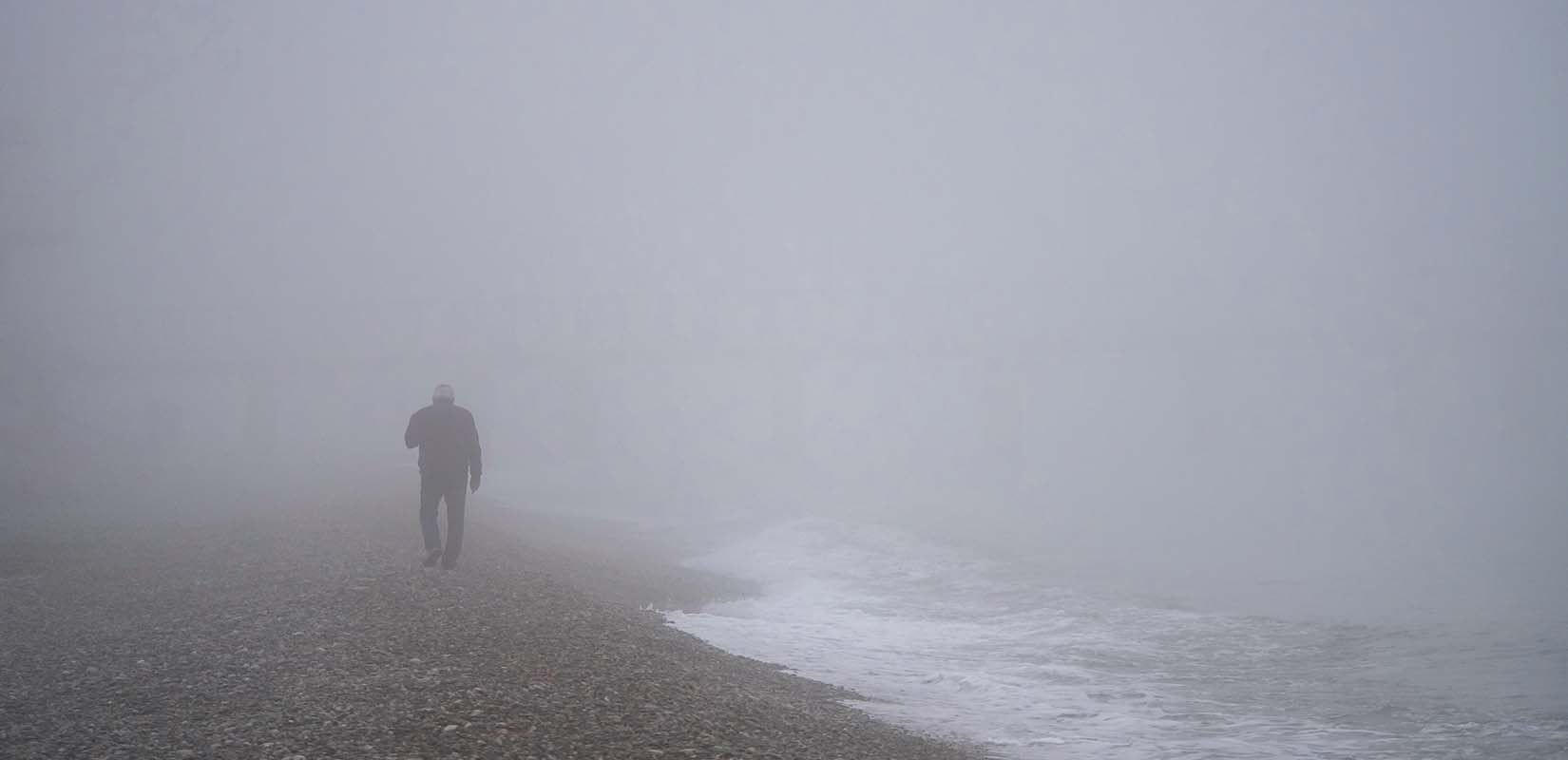 Trabajador caminando en la playa con niebla